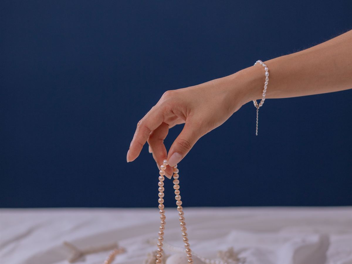 Pearl necklace lifted above white cloth (illustrative)